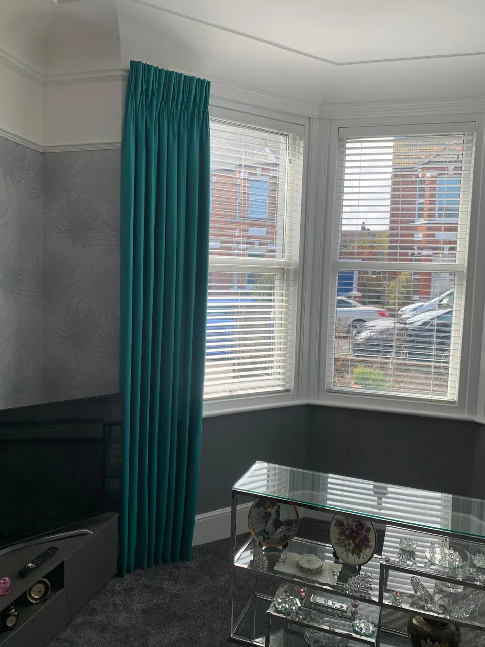 White shutters in a bay window with a teal curtain drawn to one side