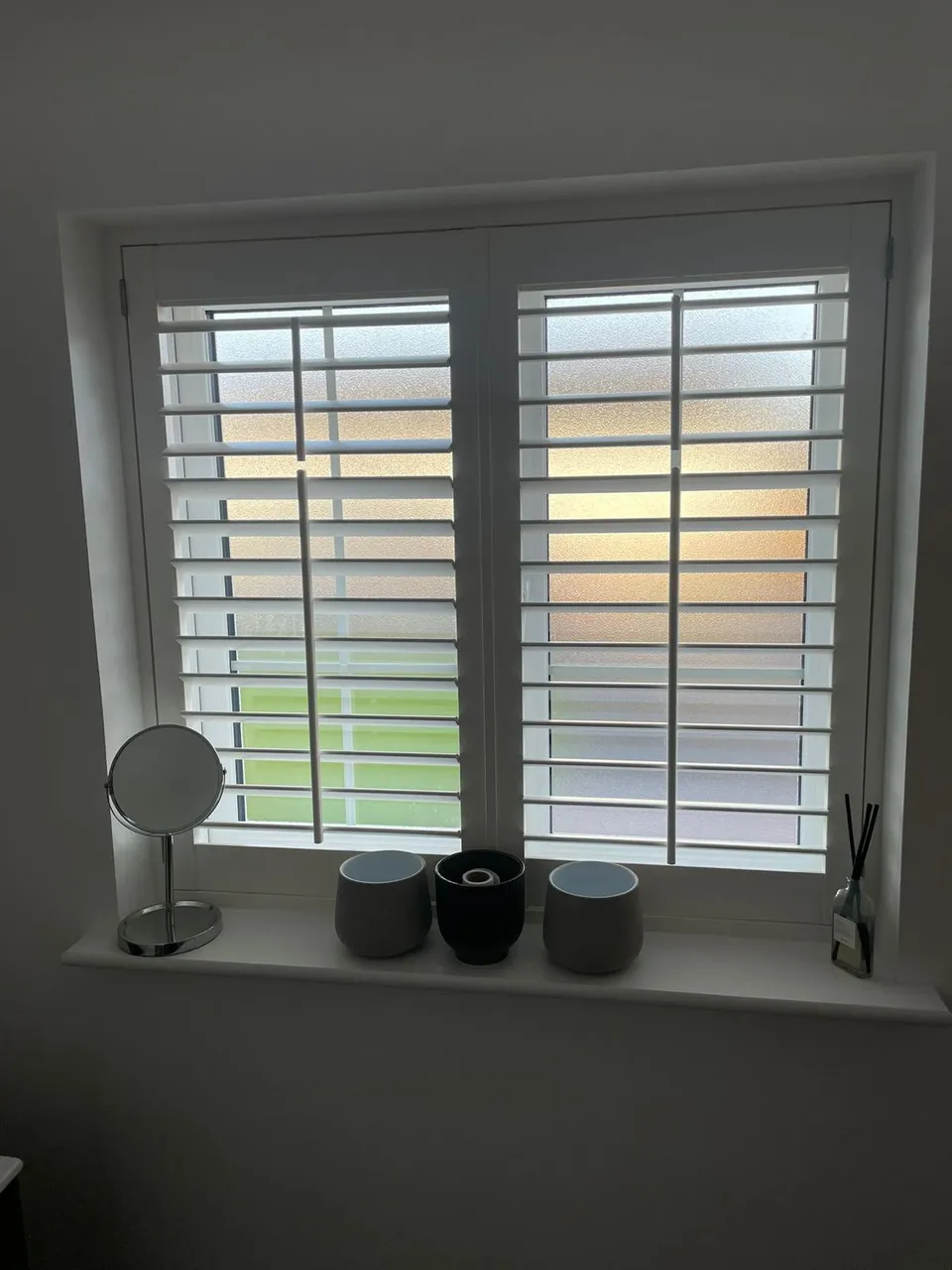 White plantation shutters on a frosted bathroom window with pots on the sill
