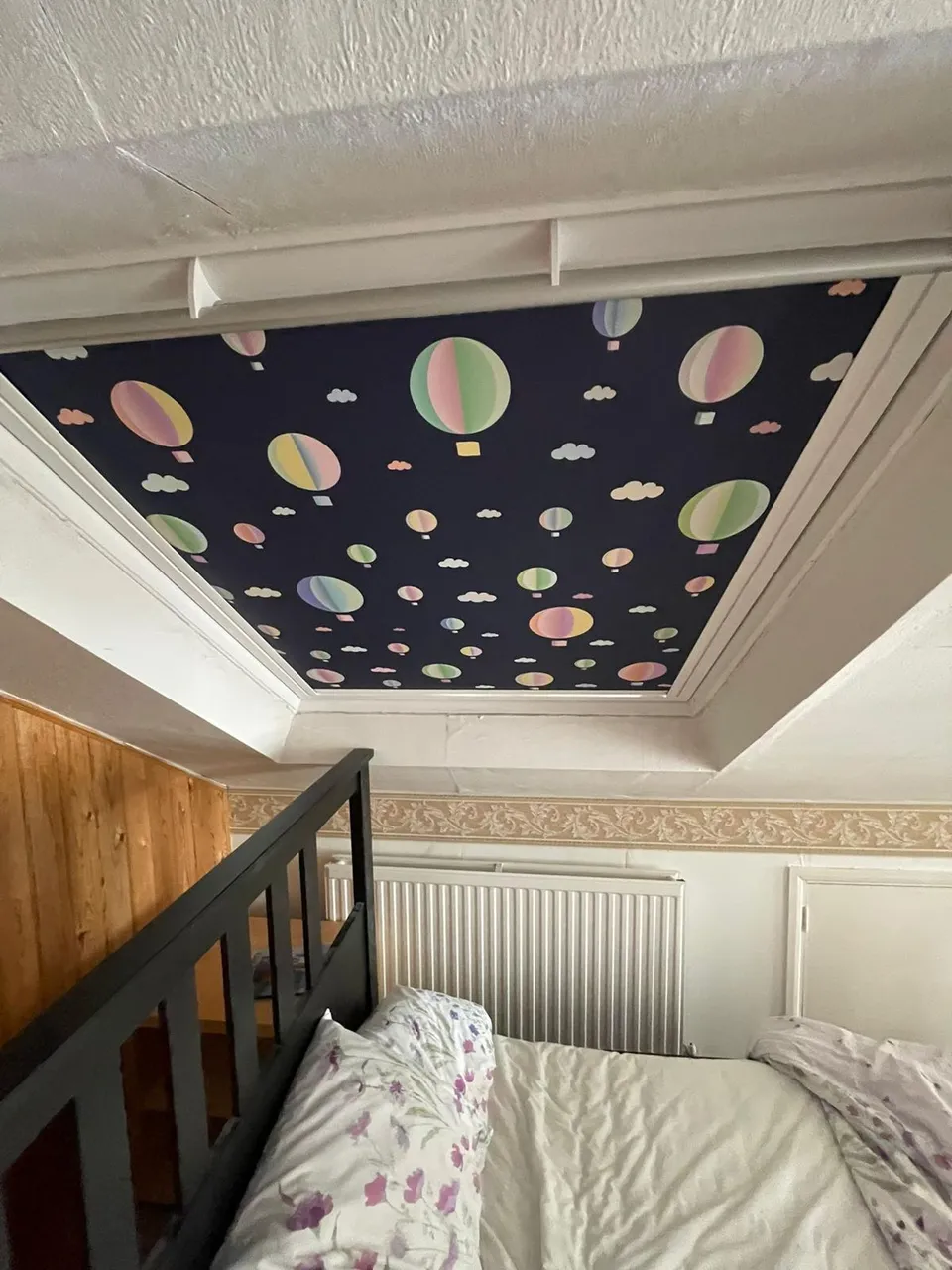 Hot air balloon print blind covering a ceiling skylight above a bed