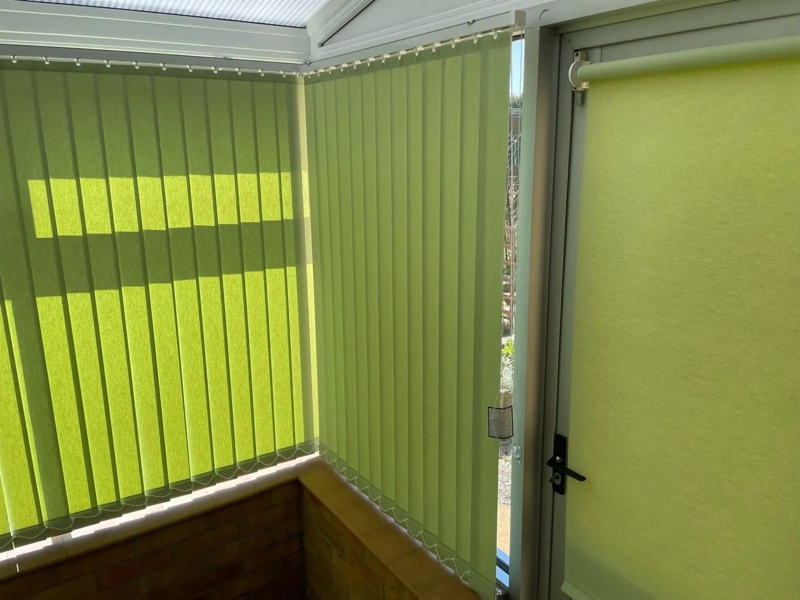 Lime green vertical blinds with a matching roller blind on the door of a conservatory